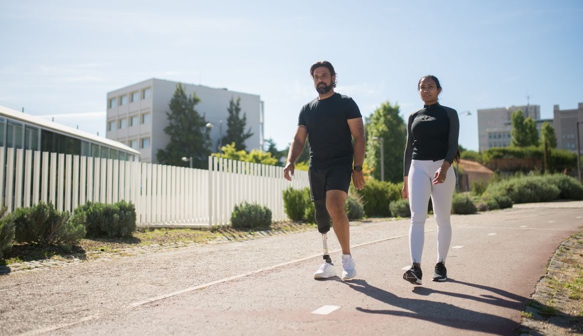 A man with a prosthetic leg and a woman walking in a sunny park path in Portugal.