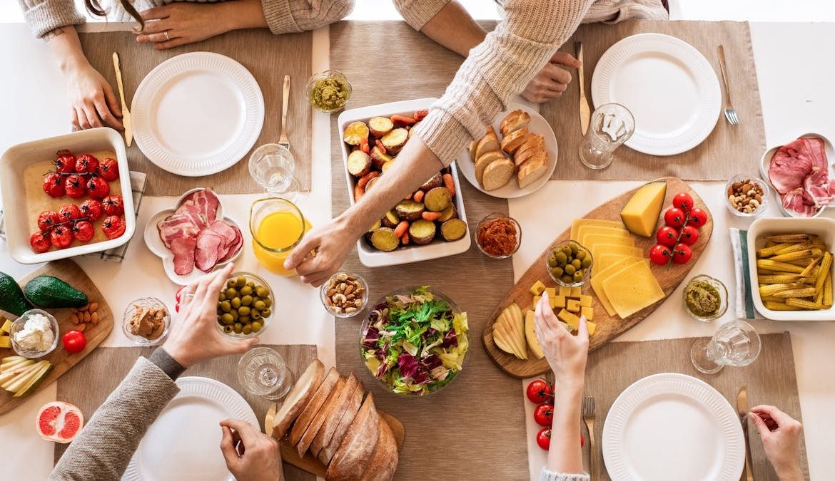 Overhead view of a diverse cheese platter setup for a delicious meal, featuring fresh produce and juices on a table.